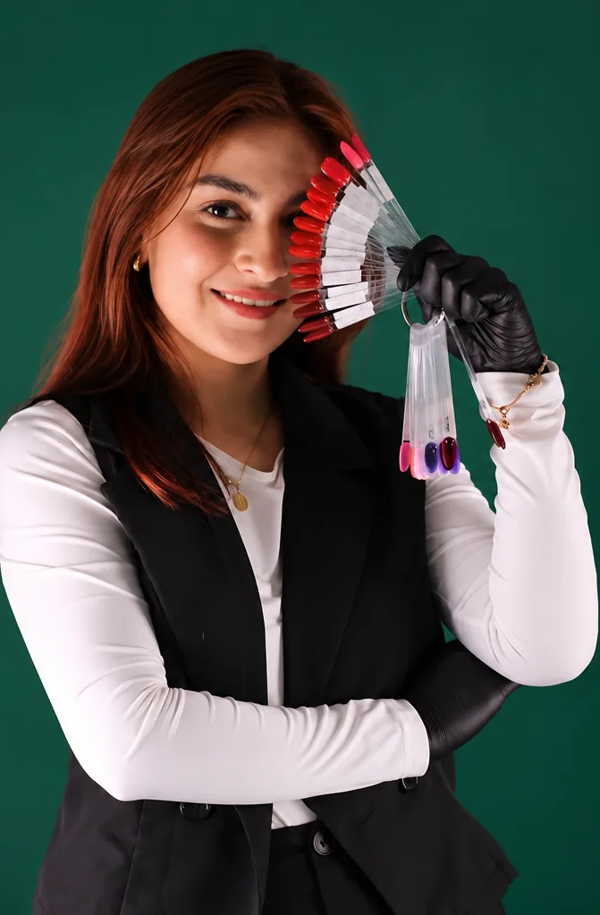 Korina sonriendo con un abanico de muestras de esmalte rojo junto al rostro y guantes negros