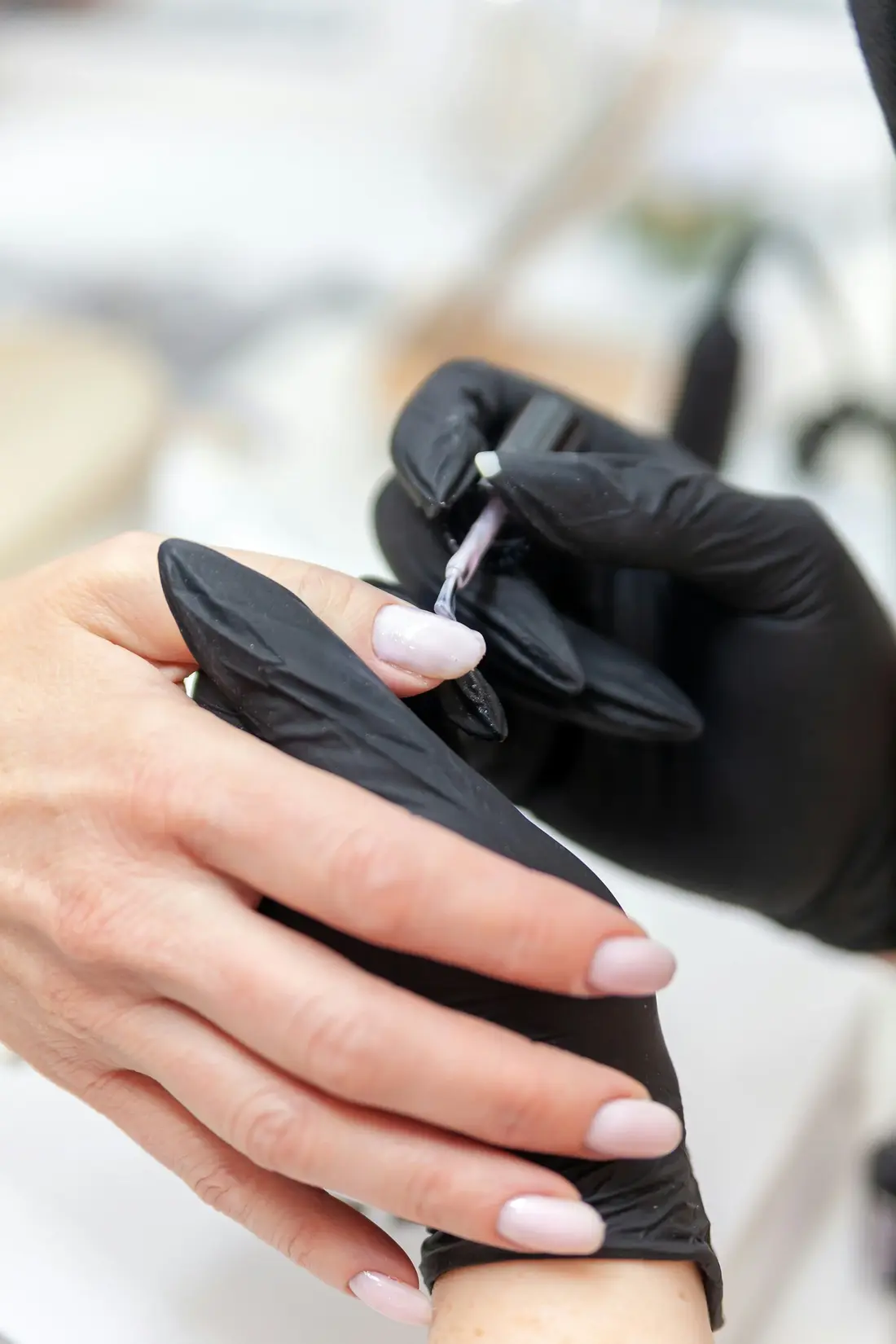 Aplicación de gel sobre la uña con guantes negros durante el servicio