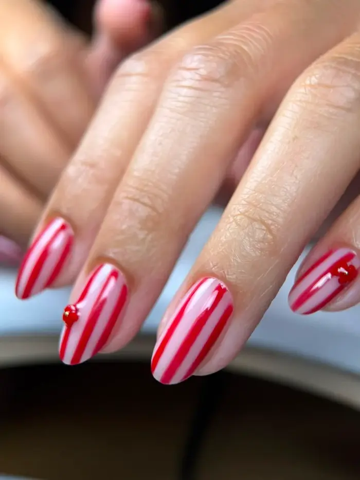 Uñas con diseño de rayas rojas y blancas sobre fondo azul